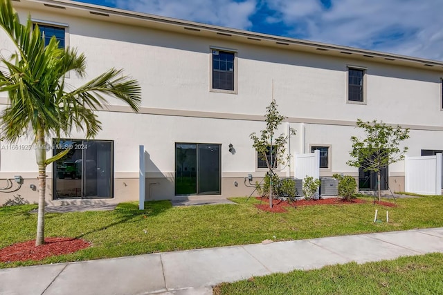 rear view of property featuring stucco siding, fence, and a yard