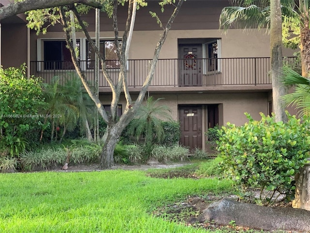 back of property featuring stucco siding, a yard, and a balcony
