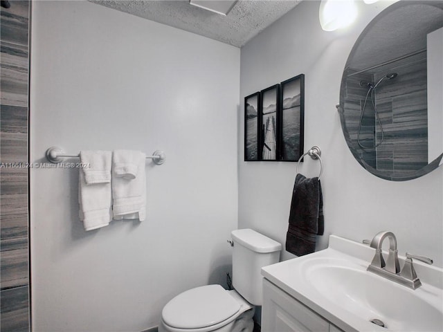 bathroom with vanity, toilet, a textured ceiling, and tiled shower