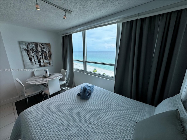 tiled bedroom with a textured ceiling, track lighting, and a water view