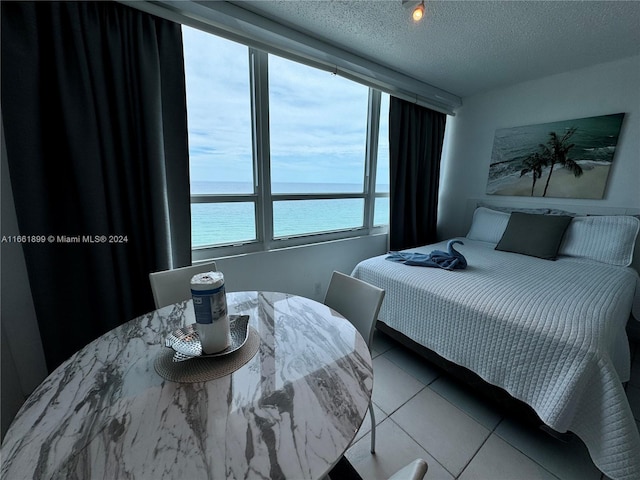 bedroom featuring a water view, a textured ceiling, and tile patterned floors