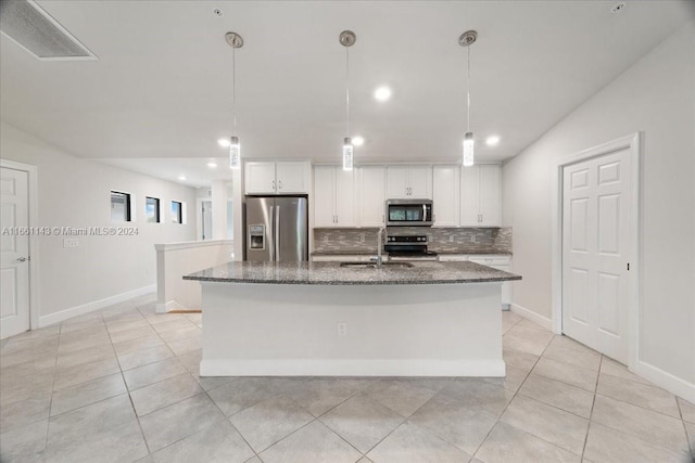 kitchen featuring appliances with stainless steel finishes, dark stone countertops, an island with sink, white cabinets, and pendant lighting