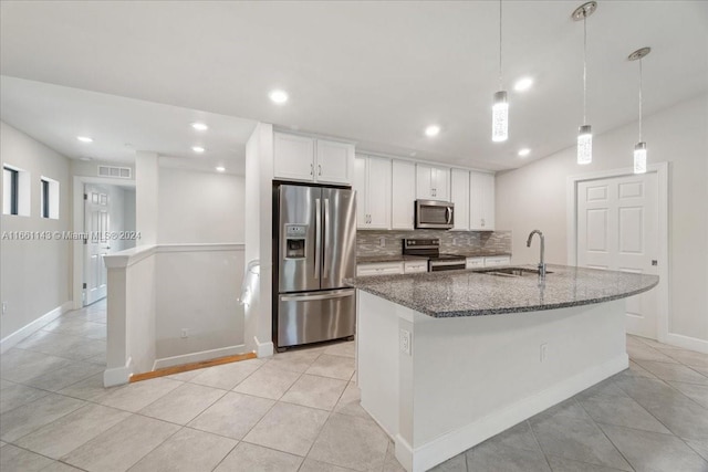 kitchen featuring an island with sink, sink, white cabinetry, stainless steel appliances, and dark stone counters