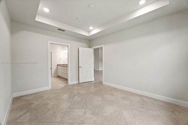 unfurnished bedroom with a raised ceiling and connected bathroom