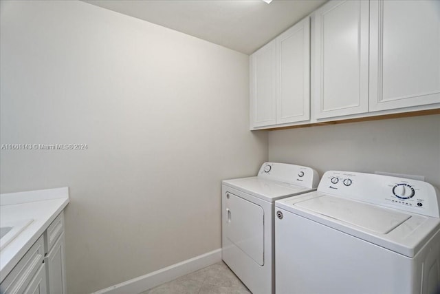 clothes washing area featuring light tile patterned flooring, washer and dryer, and cabinets