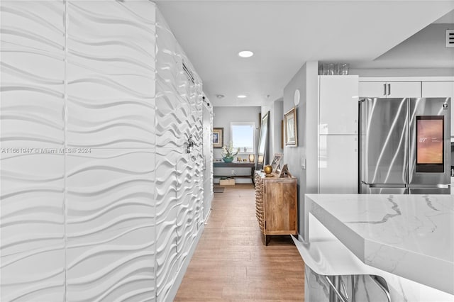 kitchen with stainless steel fridge, white cabinetry, light stone countertops, and hardwood / wood-style flooring