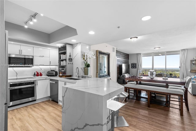 kitchen with light wood-type flooring, sink, white cabinetry, kitchen peninsula, and appliances with stainless steel finishes