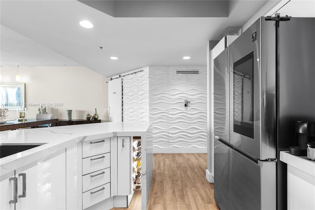 kitchen with light stone counters, kitchen peninsula, light hardwood / wood-style flooring, white cabinetry, and stainless steel refrigerator