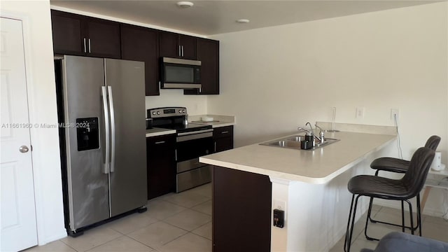 kitchen with kitchen peninsula, appliances with stainless steel finishes, a breakfast bar, dark brown cabinetry, and sink