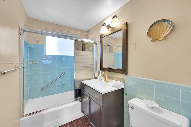 full bathroom featuring vanity, bath / shower combo with glass door, hardwood / wood-style flooring, tile walls, and toilet