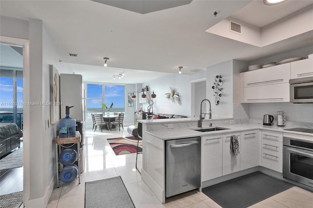 kitchen featuring sink, light tile patterned floors, kitchen peninsula, white cabinets, and appliances with stainless steel finishes