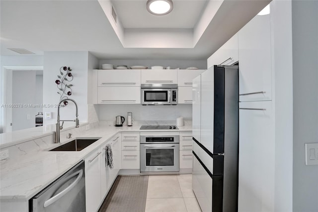 kitchen featuring a raised ceiling, sink, light stone counters, white cabinetry, and stainless steel appliances