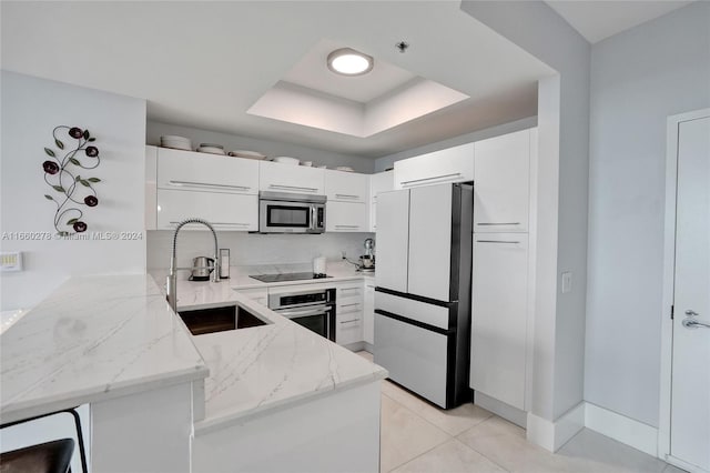 kitchen with kitchen peninsula, light stone counters, stainless steel appliances, sink, and white cabinetry