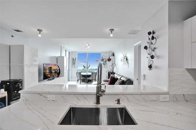 kitchen with white cabinets, light stone counters, and sink