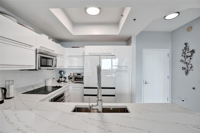 kitchen featuring light stone countertops, white cabinetry, sink, stainless steel appliances, and a raised ceiling