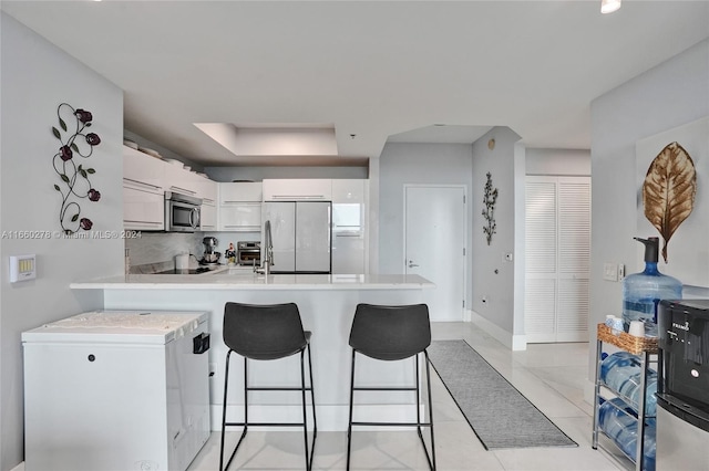 kitchen featuring kitchen peninsula, light tile patterned floors, fridge, a kitchen bar, and white cabinetry