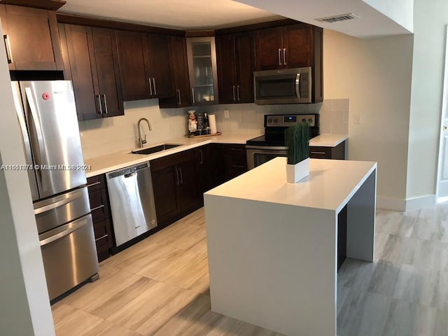 kitchen featuring backsplash, stainless steel appliances, a center island, dark brown cabinetry, and sink