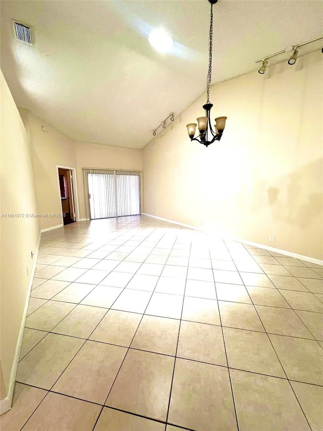 empty room with track lighting, an inviting chandelier, lofted ceiling, and light tile patterned flooring