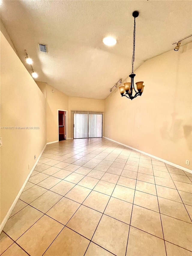 tiled spare room featuring a textured ceiling, rail lighting, a chandelier, and vaulted ceiling