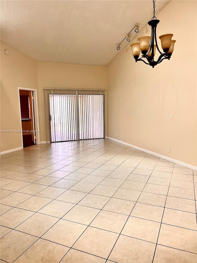 tiled empty room featuring lofted ceiling, rail lighting, a chandelier, and a textured ceiling