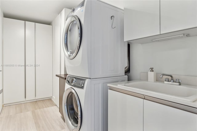 clothes washing area with cabinets, light wood-type flooring, stacked washer and clothes dryer, and sink