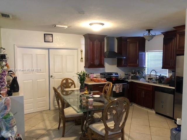 kitchen featuring appliances with stainless steel finishes, wall chimney exhaust hood, sink, and light tile patterned floors