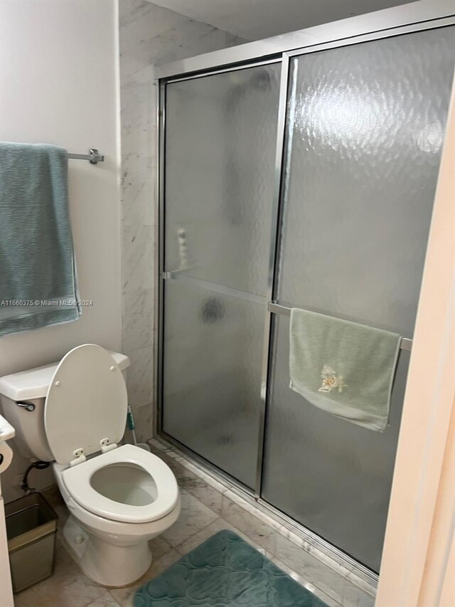 bathroom with toilet, tile patterned floors, and a shower with shower door