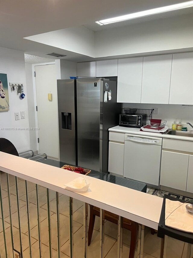 kitchen with white dishwasher, white cabinetry, and sink