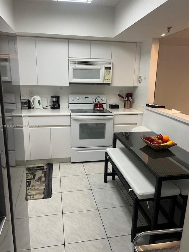 kitchen with white appliances, light tile patterned floors, washer / dryer, and white cabinets