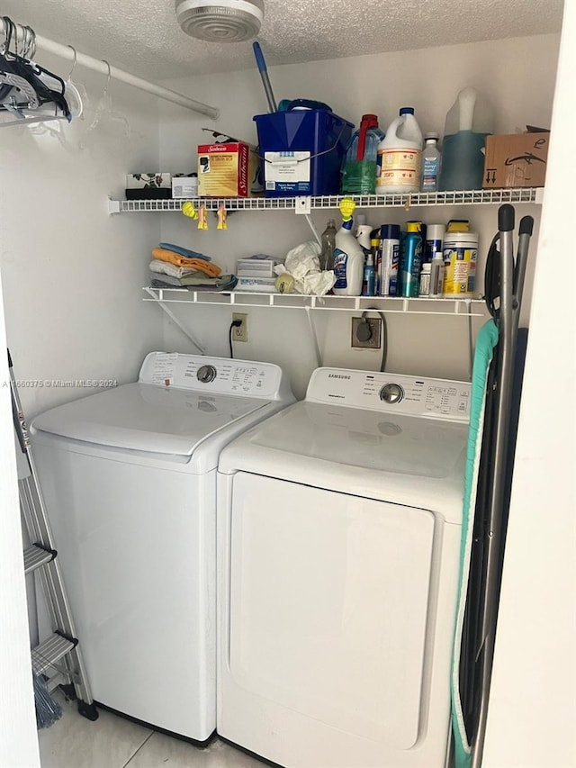 clothes washing area featuring a textured ceiling, light tile patterned floors, and washing machine and dryer