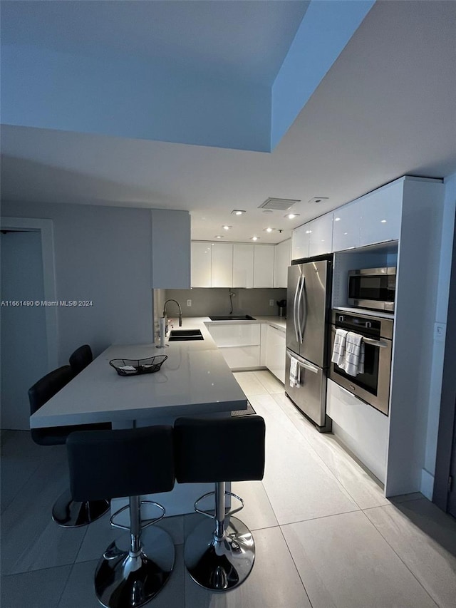 kitchen with a breakfast bar area, stainless steel appliances, sink, and white cabinetry