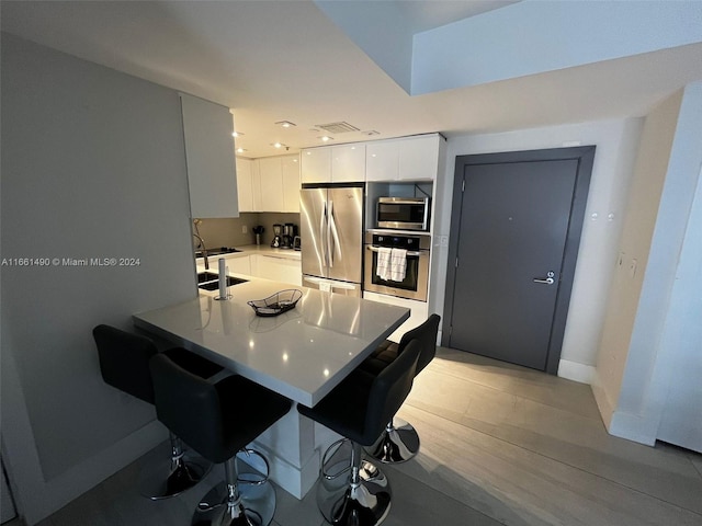 kitchen with sink, kitchen peninsula, white cabinetry, appliances with stainless steel finishes, and a breakfast bar