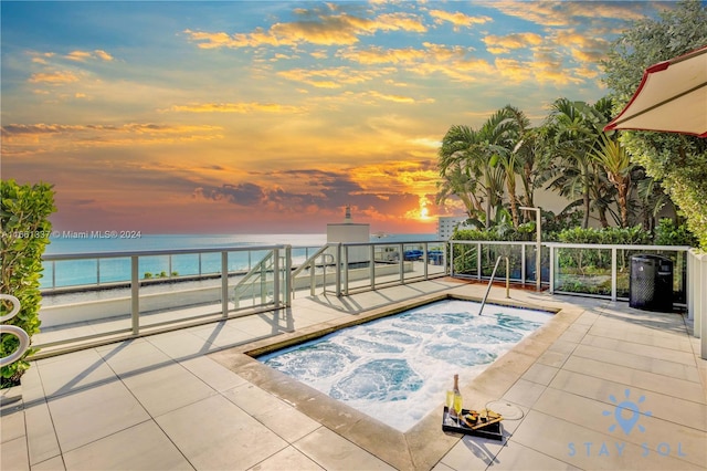 pool at dusk with a water view and an in ground hot tub