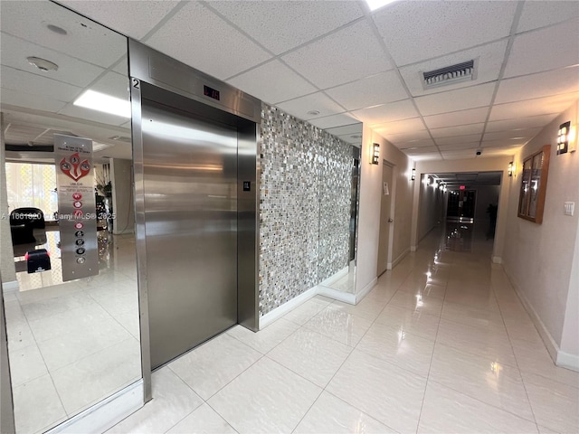 corridor with a drop ceiling, light tile patterned flooring, and elevator