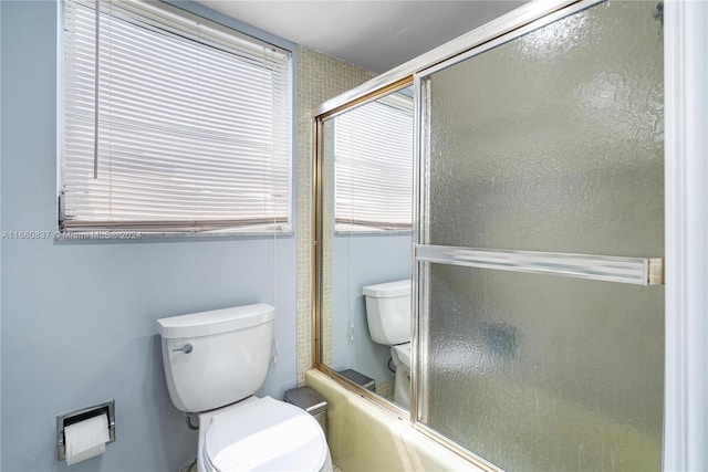 bathroom featuring combined bath / shower with glass door and toilet