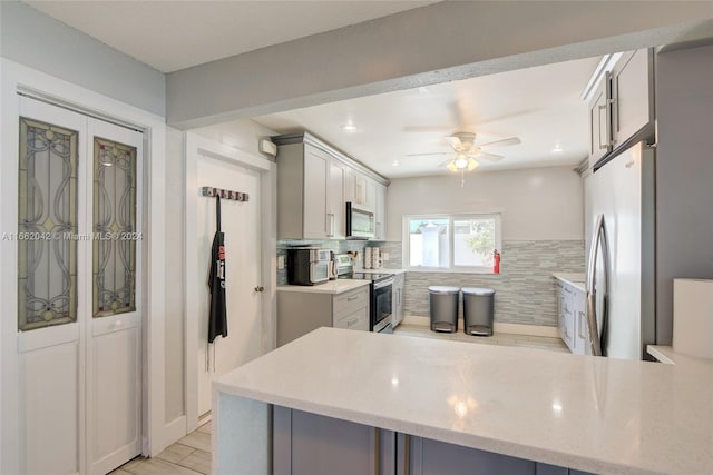 kitchen with ceiling fan, kitchen peninsula, gray cabinetry, backsplash, and appliances with stainless steel finishes