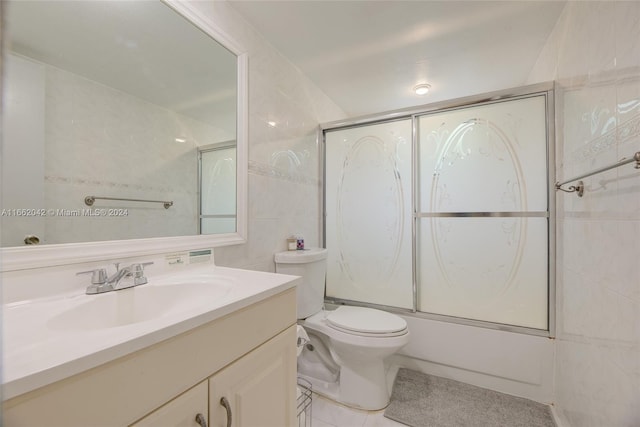 full bathroom featuring tile walls, tile patterned flooring, shower / bath combination with glass door, vanity, and toilet