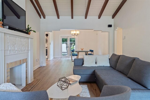 living room with beam ceiling, stacked washer / dryer, light hardwood / wood-style floors, and an inviting chandelier