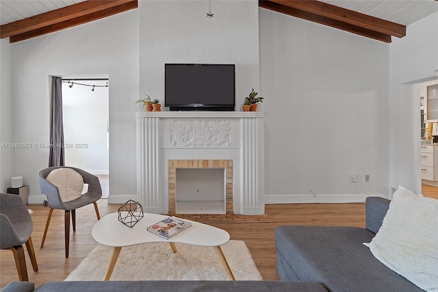 living room with lofted ceiling with beams, a brick fireplace, wood ceiling, and light wood-type flooring