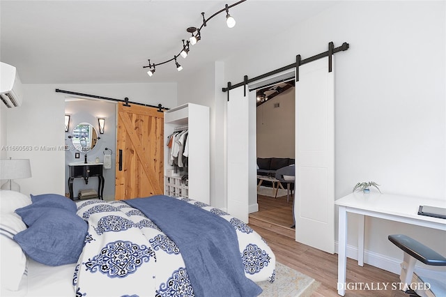 bedroom with vaulted ceiling, rail lighting, a wall mounted AC, hardwood / wood-style flooring, and a barn door