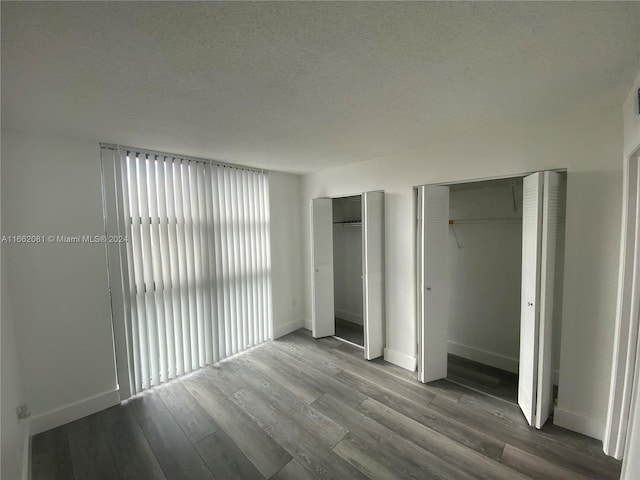 unfurnished bedroom featuring multiple closets, hardwood / wood-style floors, and a textured ceiling