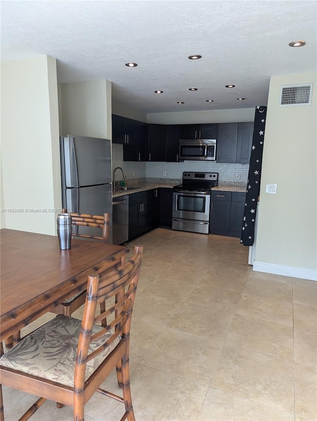 kitchen with appliances with stainless steel finishes, a textured ceiling, sink, and tasteful backsplash