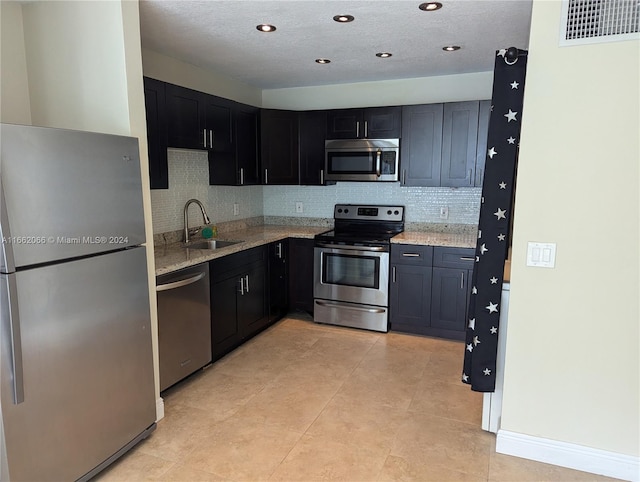 kitchen with appliances with stainless steel finishes, light stone counters, backsplash, a textured ceiling, and sink