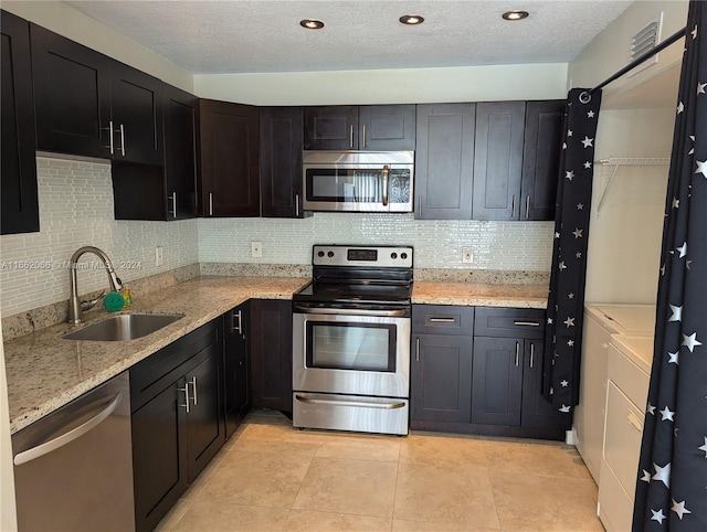 kitchen featuring sink, washing machine and clothes dryer, a textured ceiling, appliances with stainless steel finishes, and light stone countertops