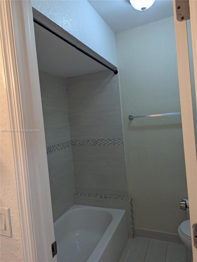 bathroom with tiled shower / bath, toilet, and tile patterned floors