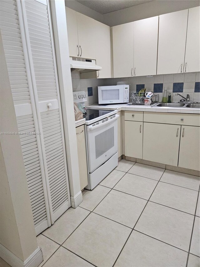 kitchen with tasteful backsplash, sink, light tile patterned floors, and white appliances