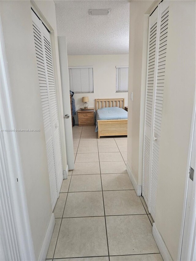 corridor featuring a textured ceiling and light tile patterned flooring