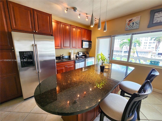 kitchen with light tile patterned flooring, hanging light fixtures, a kitchen breakfast bar, appliances with stainless steel finishes, and dark stone countertops