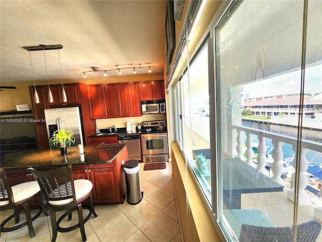 kitchen featuring light tile patterned flooring, hanging light fixtures, sink, stainless steel appliances, and dark stone counters