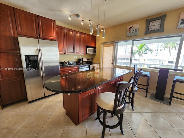 kitchen featuring light tile patterned flooring, hanging light fixtures, a kitchen island, appliances with stainless steel finishes, and dark stone countertops